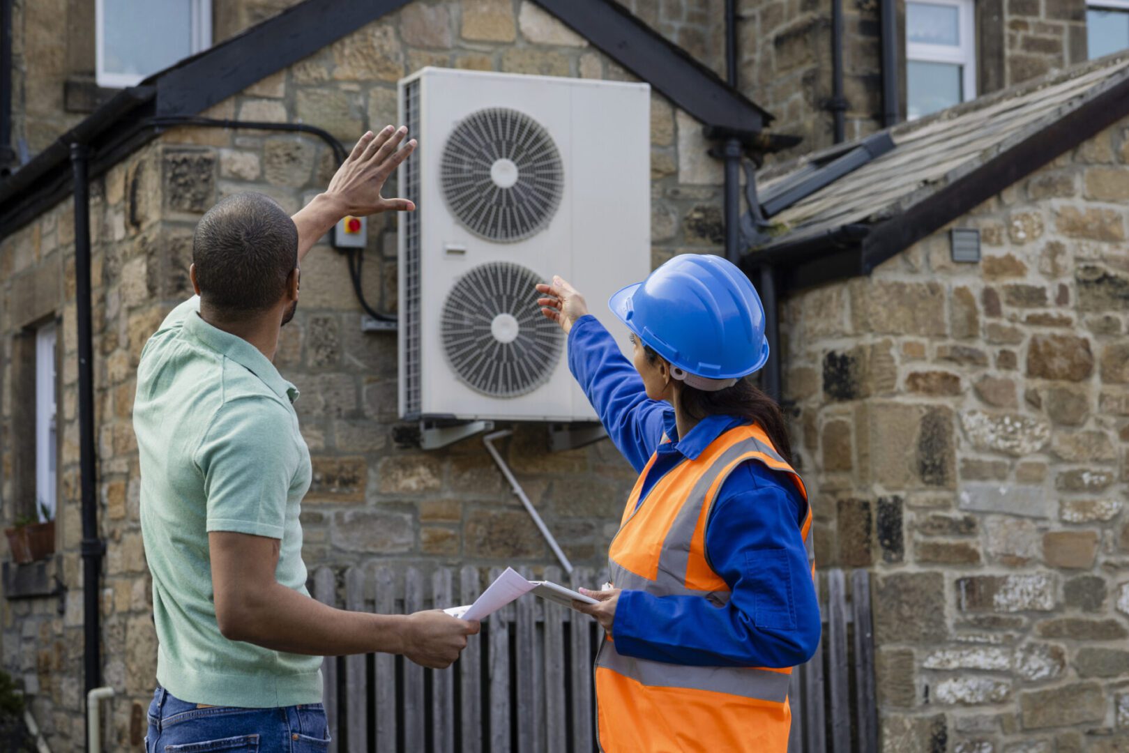 Technician explaining air conditioner unit to homeowner outdoors.