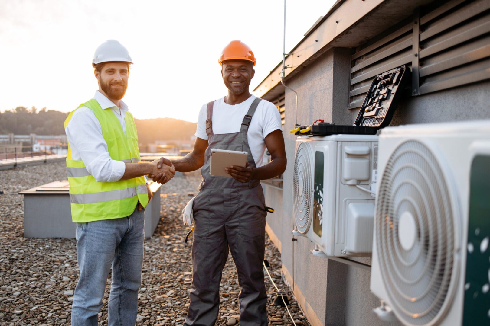 Two workers shaking hands at an industrial site with HVAC equipment.